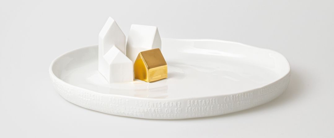 Porzellangeschichten Teller mit Häusern: Drei weiße Häuser und ein goldenes Haus auf einem weißen Teller.