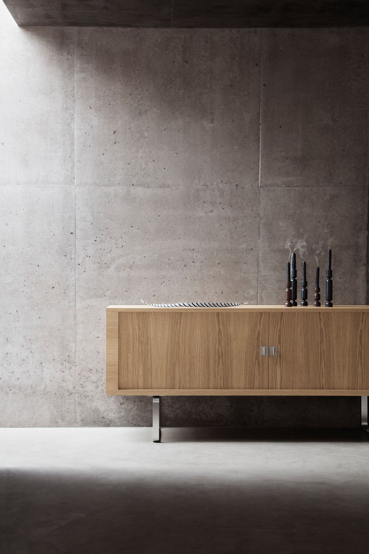 CH825 Credenza Sideboard von Carl Hansen: Holz-Anrichte mit Schiebetüren und minimalistischen Kerzenständern vor Betonwand.