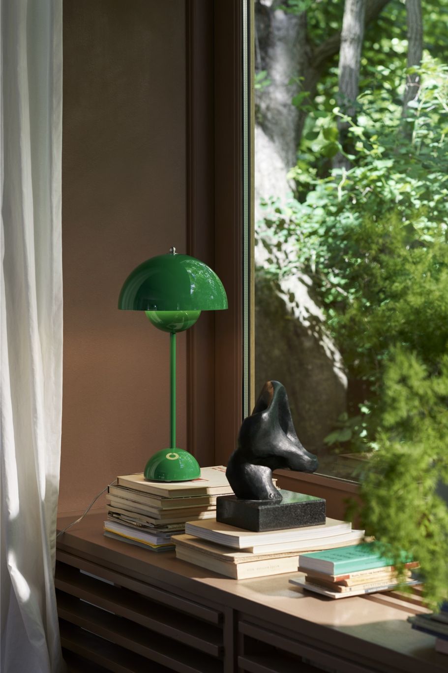 Grüne Flowerpot VP3 Tischleuchte von AndTradition auf einem Stapel Bücher, neben einem Fenster mit Blick ins Grüne.
