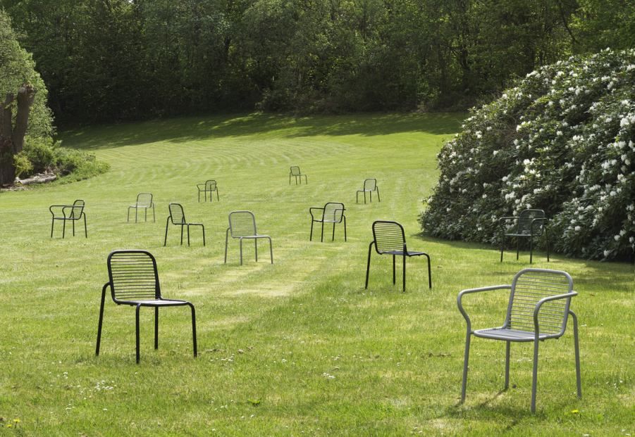 Mehrere Normann Copenhagen Vig Chair Stühle im Freien auf einem grünen Rasen mit Bäumen im Hintergrund.