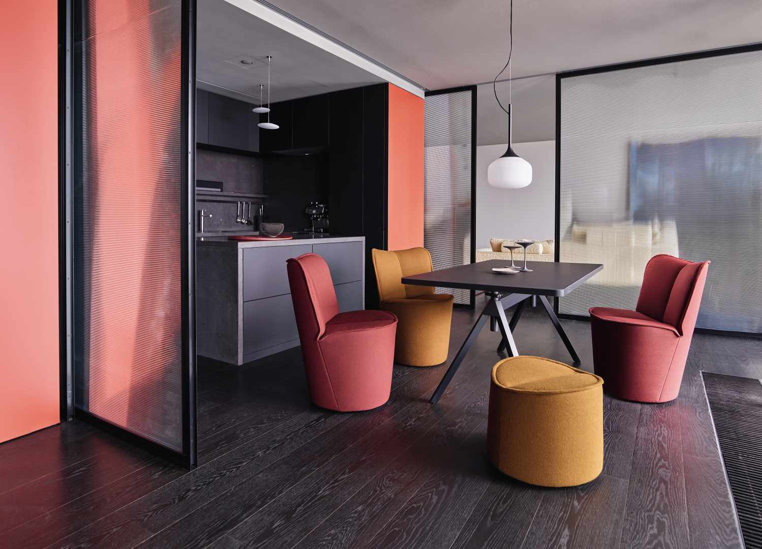 Esszimmer mit Cor Sessel in Rot und Gelb, moderner Hocker und schwarzem Tisch.