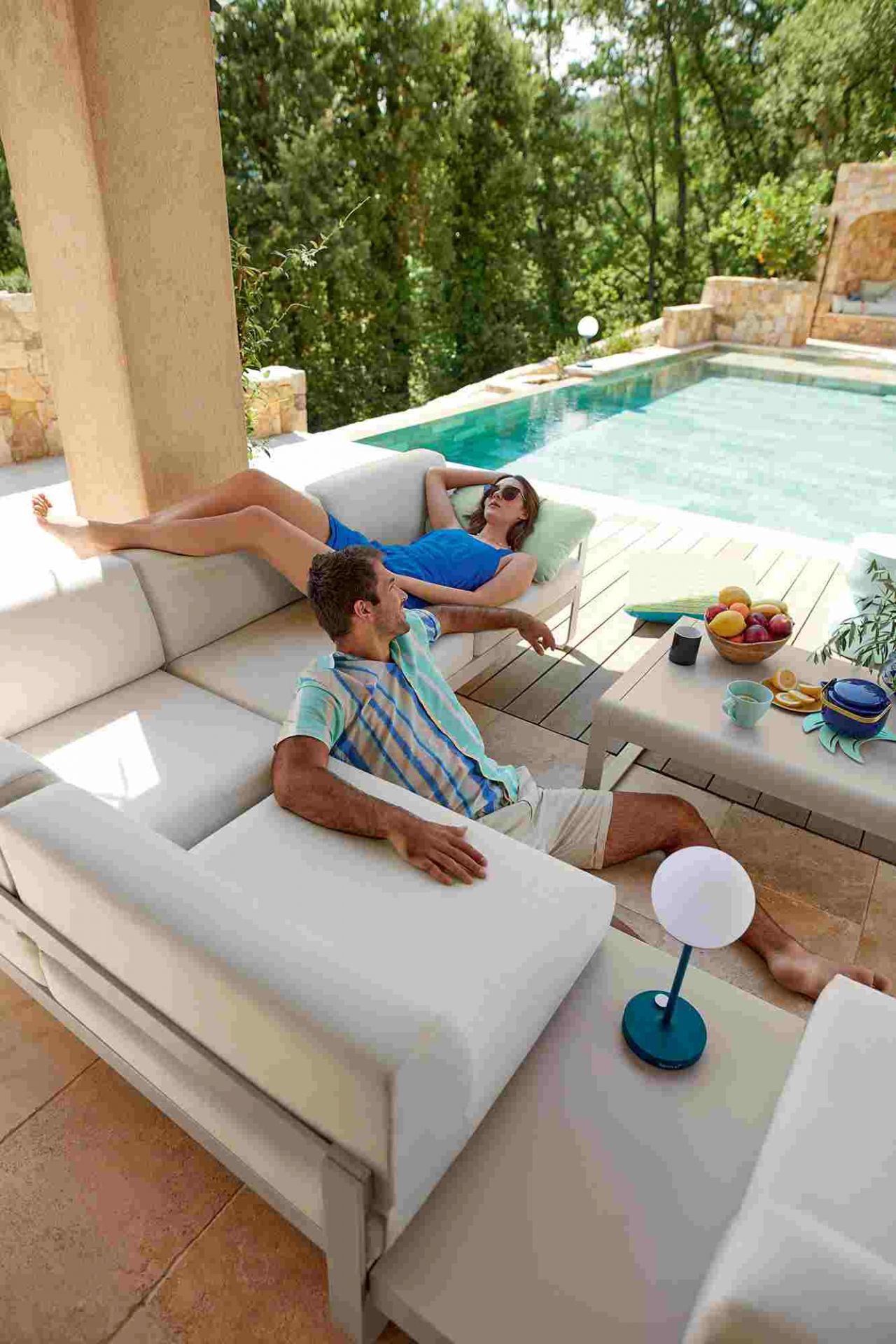 Paar entspannt am Pool mit Fermob Bellevie Outdoor Lounge Möbeln und Beistelltisch.