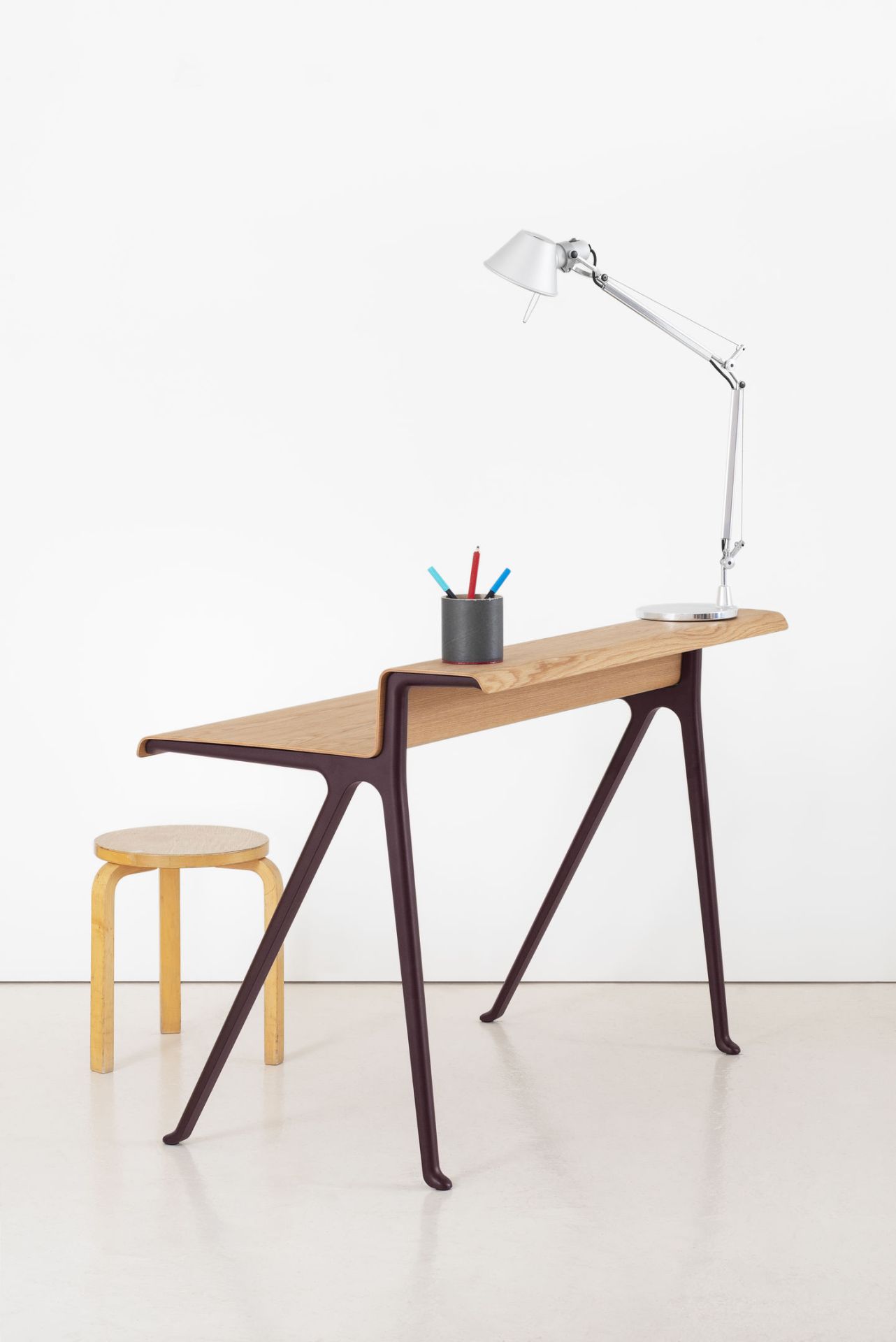 Vitra Courier Schreibtisch aus Holz mit Lampe und Hocker vor weißem Hintergrund.