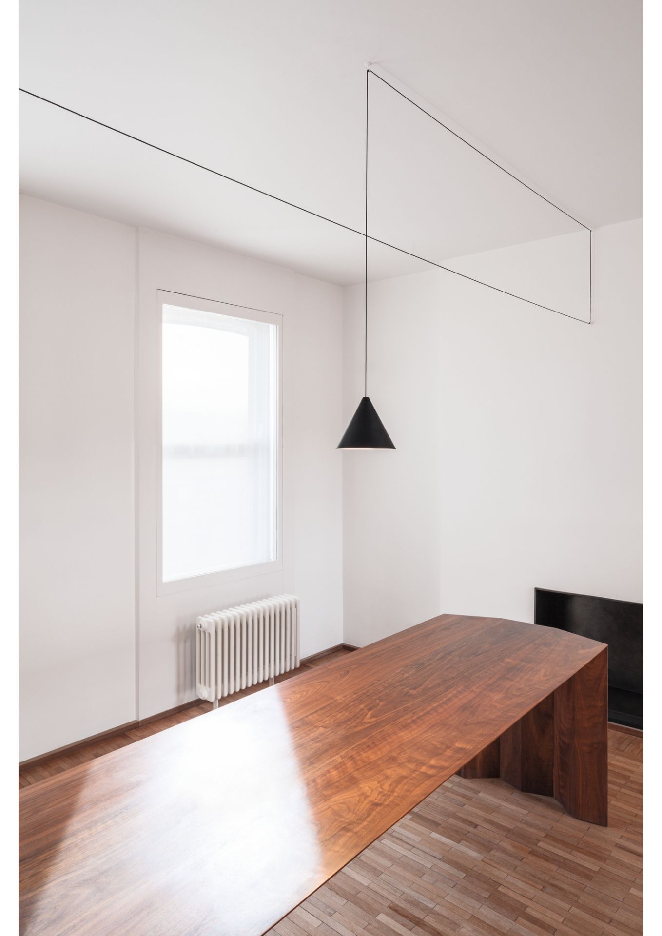 Innenaufnahme mit Flos String Light Kegelkopf Pendelleuchte über einem Holztisch.