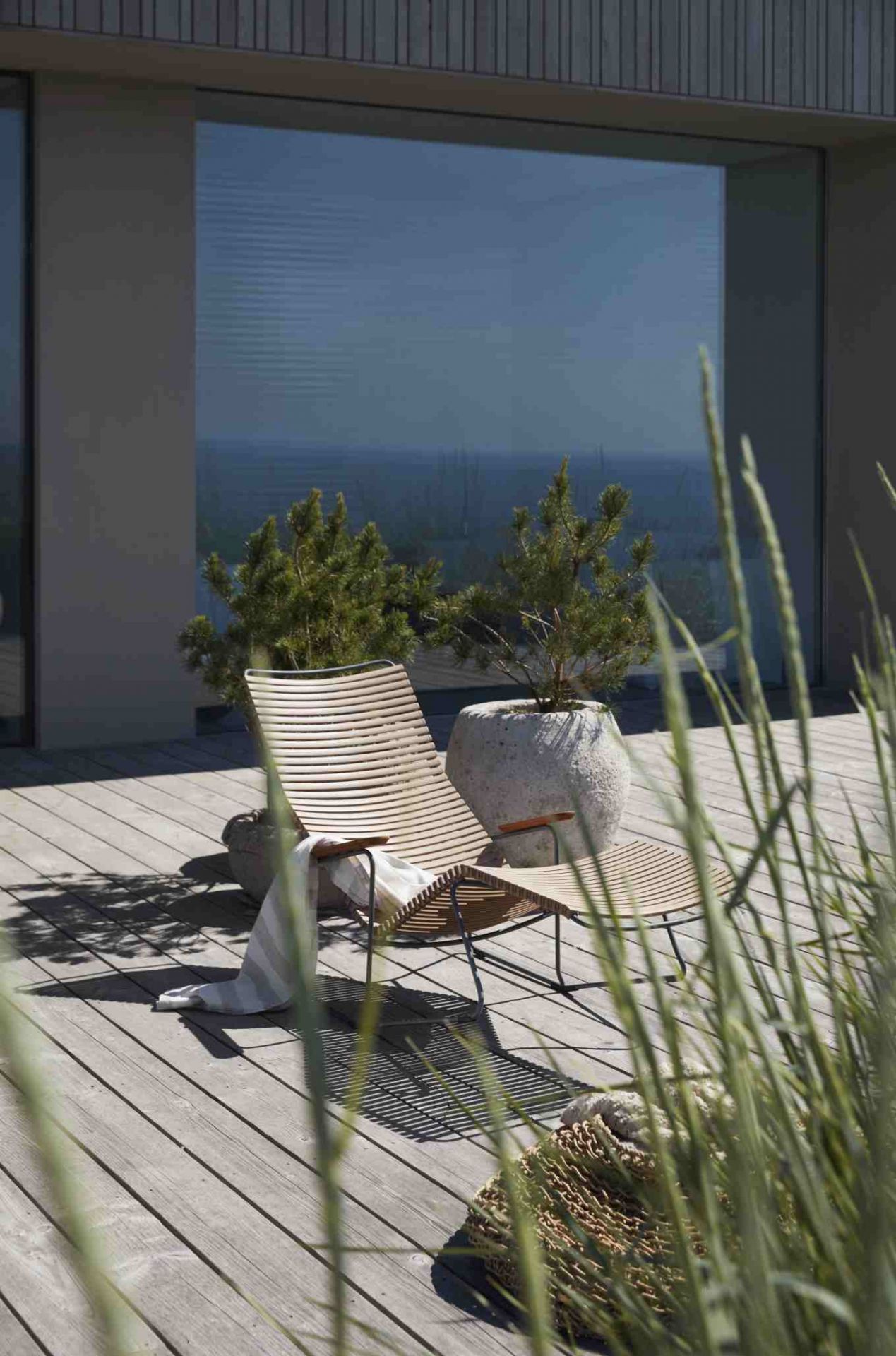 Click Sunrocker Sonnenliege von Houe in Dunkelgrau auf Holzterrasse mit Dekoration und Pflanzen.