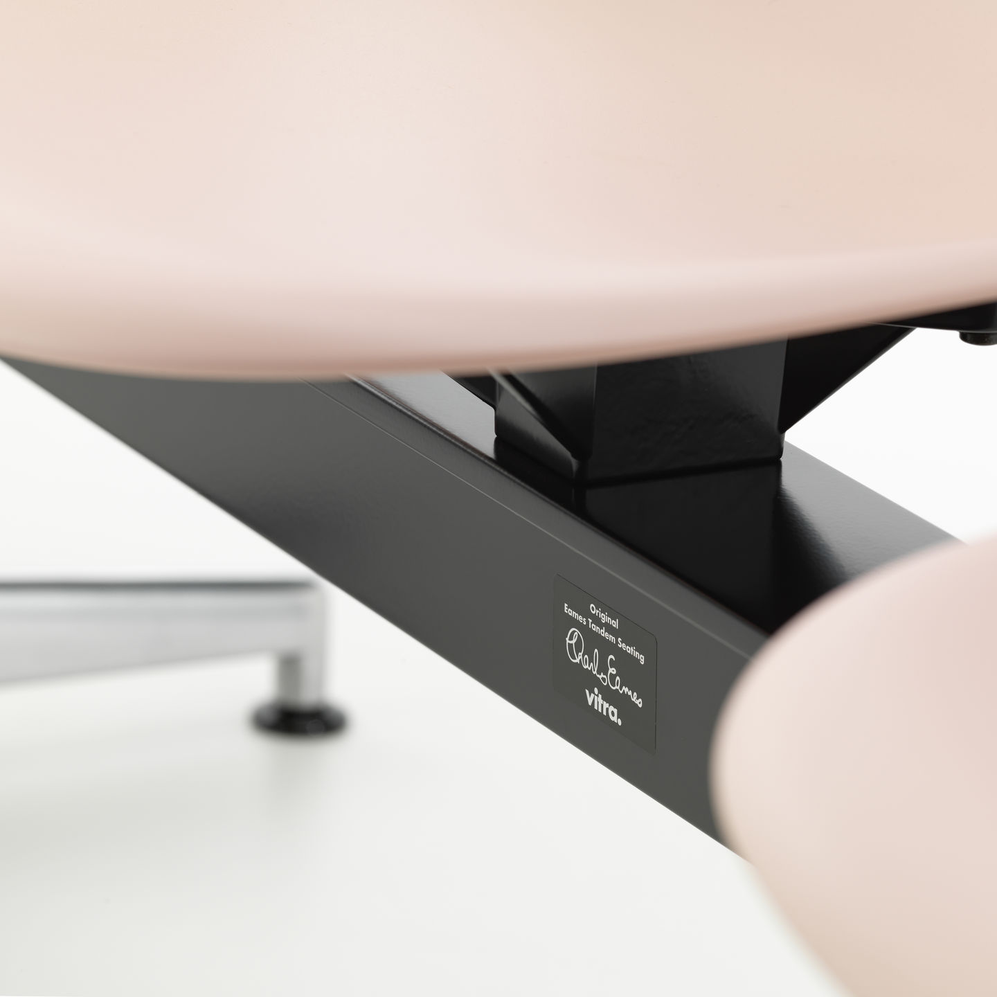 Detailaufnahme Eames Plastic Side Chair RE auf Traverse von Vitra, Sitzschale rosa, Gestell schwarz.