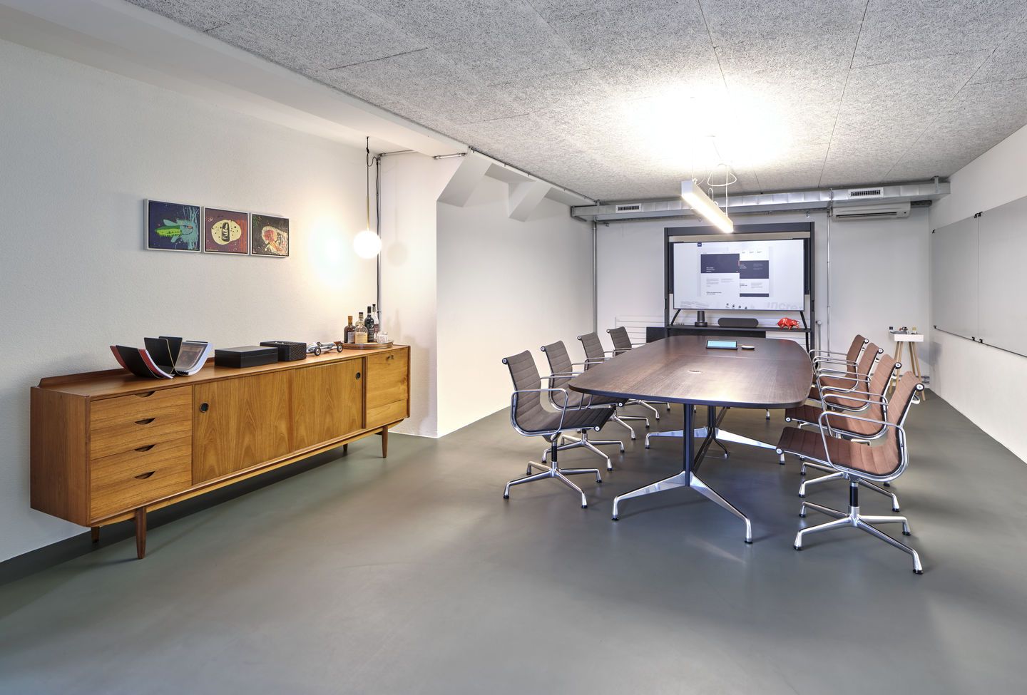 Konferenzraum mit langem Holztisch und Vitra EA 108 Aluminium Stühlen mit braunem und grauem Bezug.