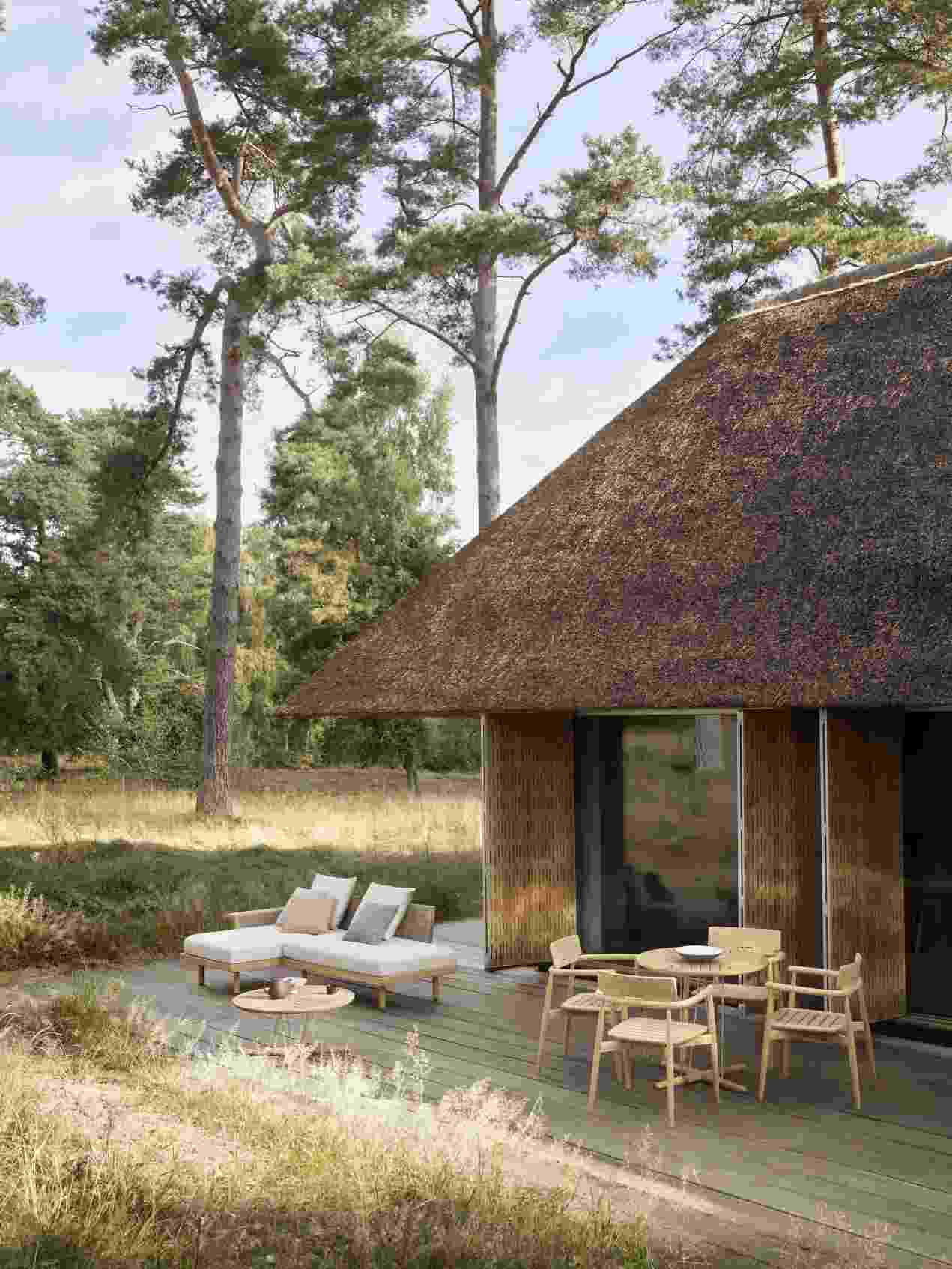 E511 Embrace Sofa Modul von Carl Hansen & Søn mit Outdoor-Möbeln und Reetdachhaus im Garten.