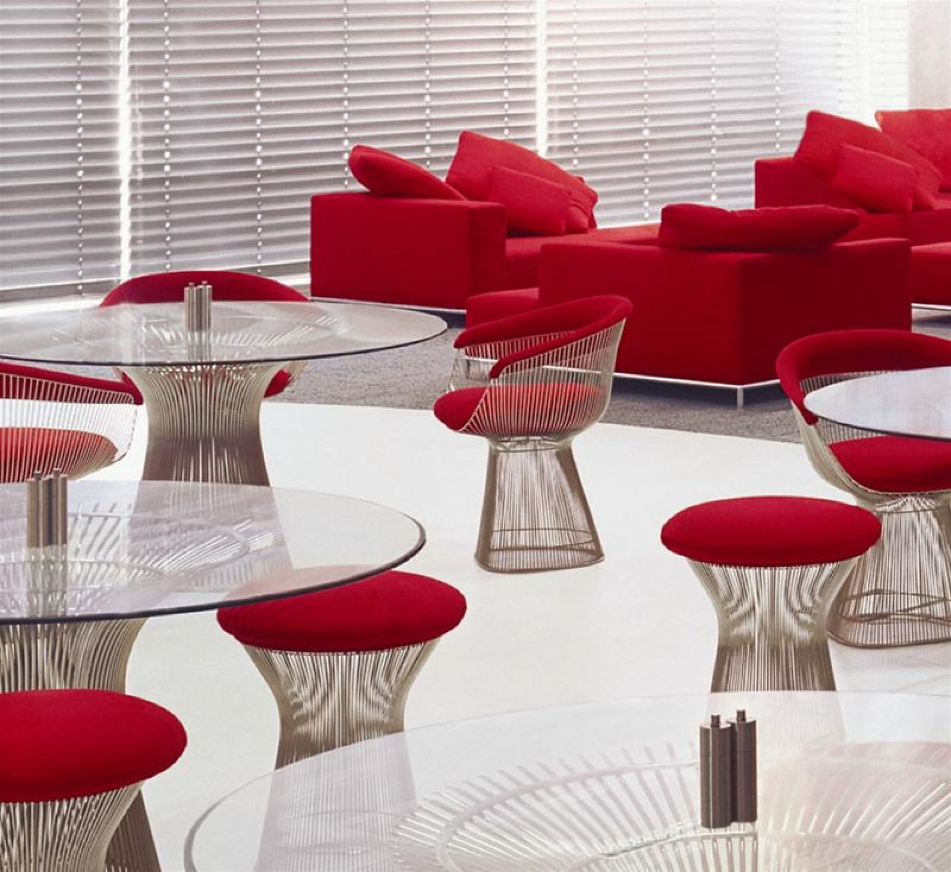 Mehrere Platner Tische von Knoll International mit Glasplatte und Drahtgestell in einem roten Lounge-Bereich.