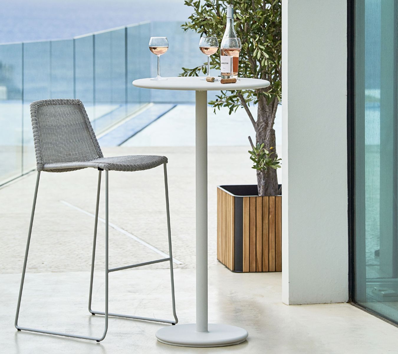 Cane-Line Combine Pflanzgefäß quadratisch aus Teakholz mit Barhocker und Bistrotisch auf einer Terrasse.