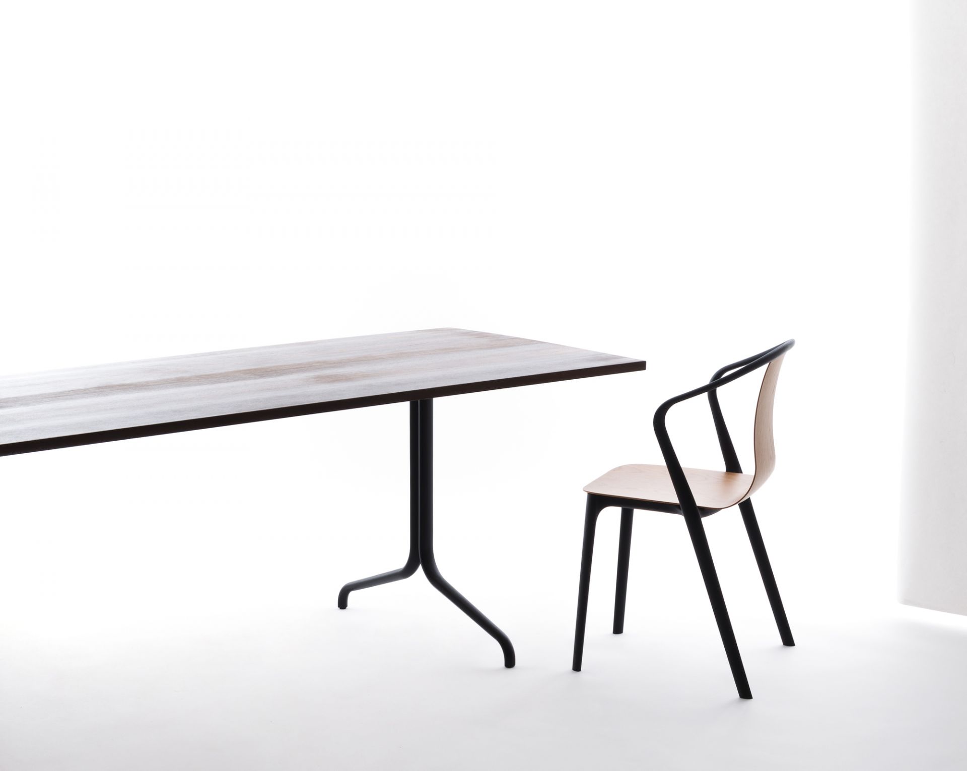Vitra Belleville Chair Plastic Stuhl neben Esstisch, minimalistisches Design mit schwarzem Gestell und hellem Holz.