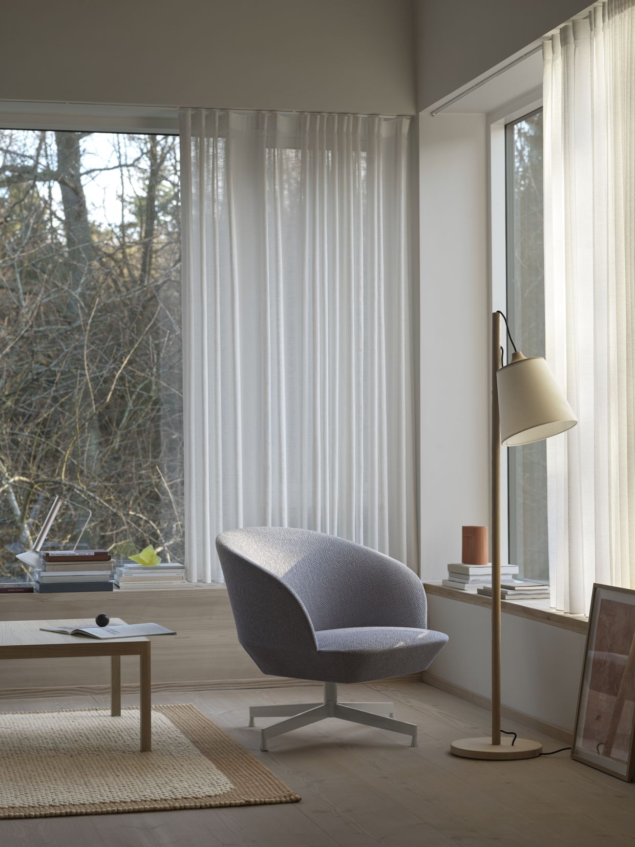 Muuto Oslo Lounge Chair Sessel in Grau mit Drehfuß, neben Stehlampe und Tisch.