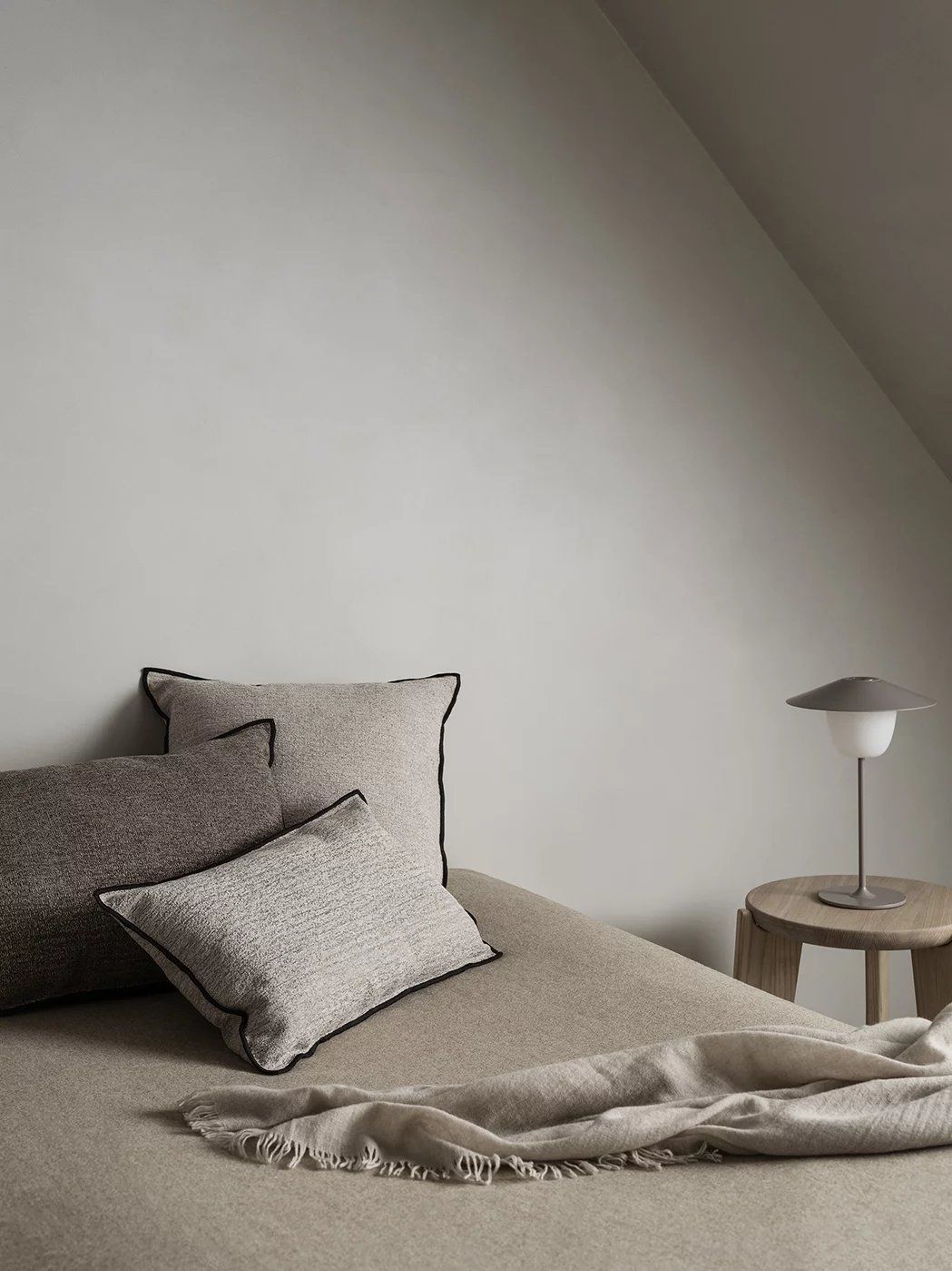 Nahaufnahme des Eli Stool Sitzhockers von Blomus, mit Kissen und Lampe auf einem Hocker.