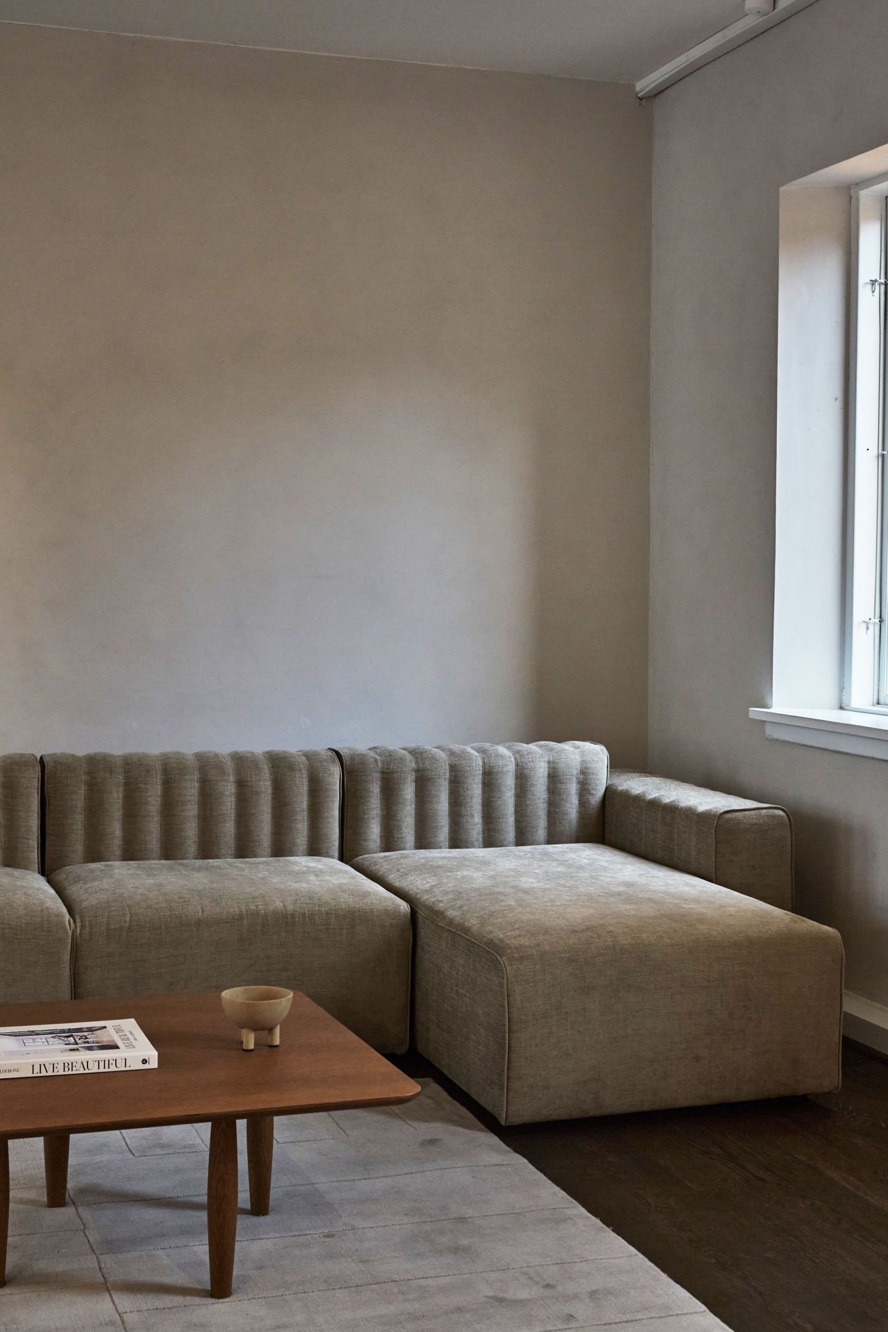 Oku Couchtisch aus geräucherter Eiche von Norr11 vor beiger Couch und Teppich.