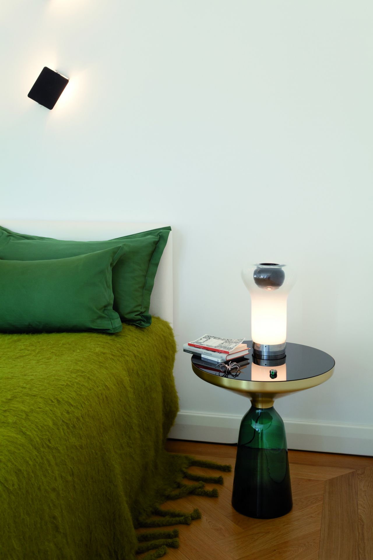 Bell Side Table Beistelltisch von ClassiCon in Bernstein-Orange neben einem Bett mit grüner Decke.