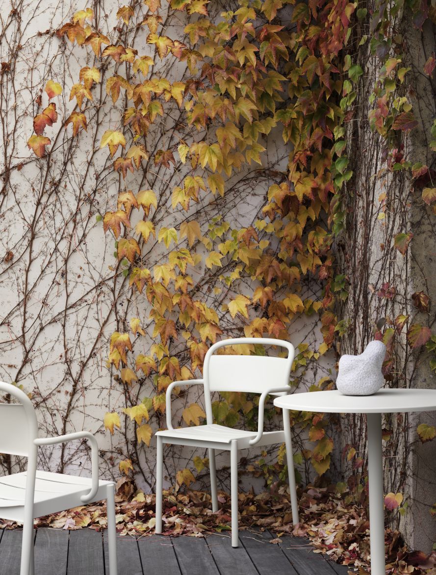 Muuto Linear Steel Beistelltisch und Stühle in Weiß vor einer Wand mit Herbstlaub. Outdoor-Möbel.