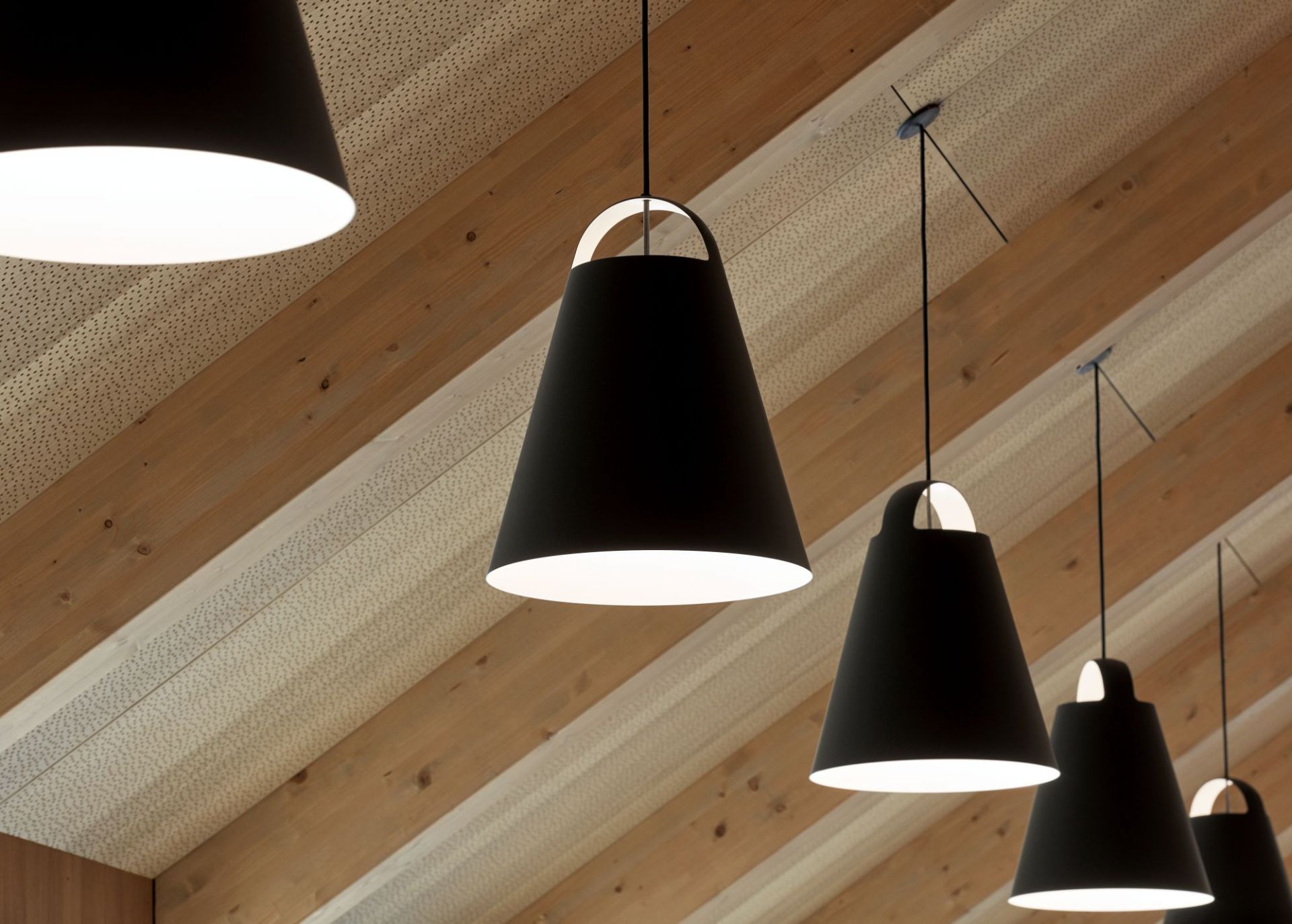 Mehrere schwarze Above Pendelleuchten von Louis Poulsen hängen vor einer Holzdecke.