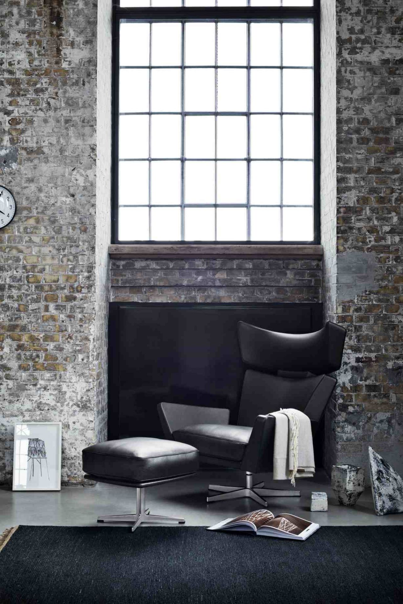 Schwarzer Oksen Sessel von Fritz Hansen mit Hocker in modernem Loft-Ambiente vor Backsteinwand.