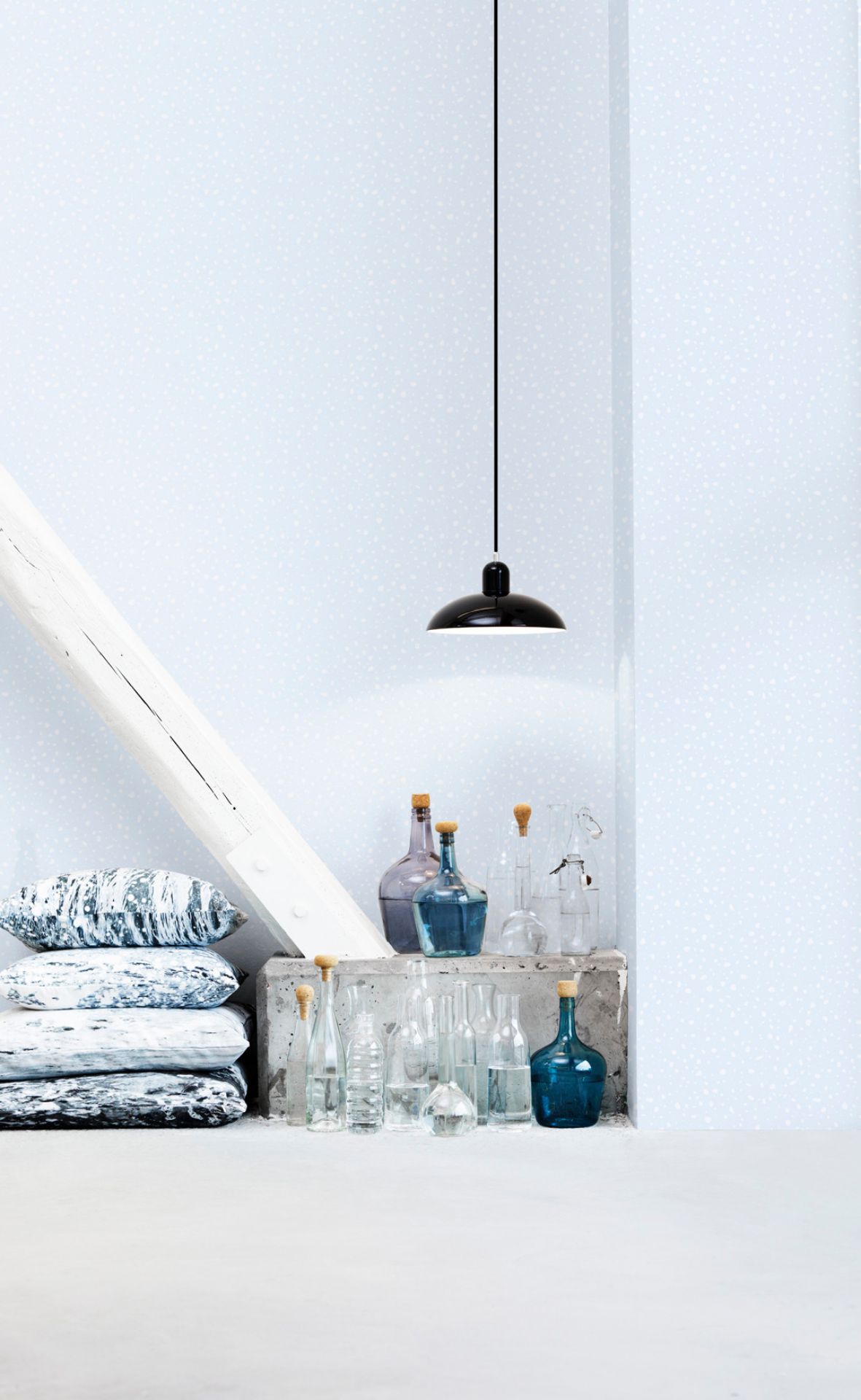 Schwarze KAISER idell Pendelleuchte 6631 P von Fritz Hansen über dekorativen Glasflaschen und Kissen.