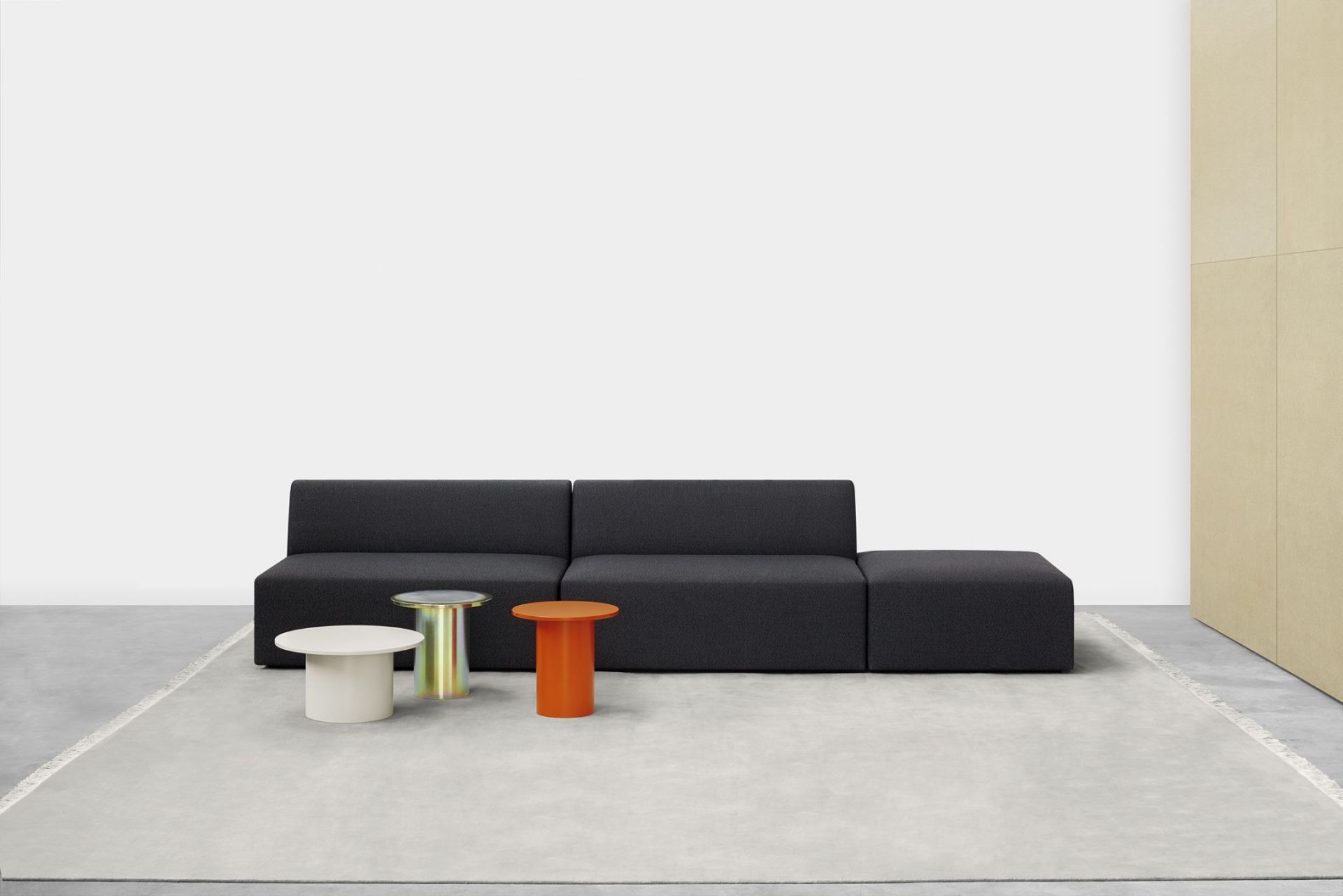Enoki Beistelltische von e15 in Weiß, Orange und Gold vor einem schwarzen Sofa.
