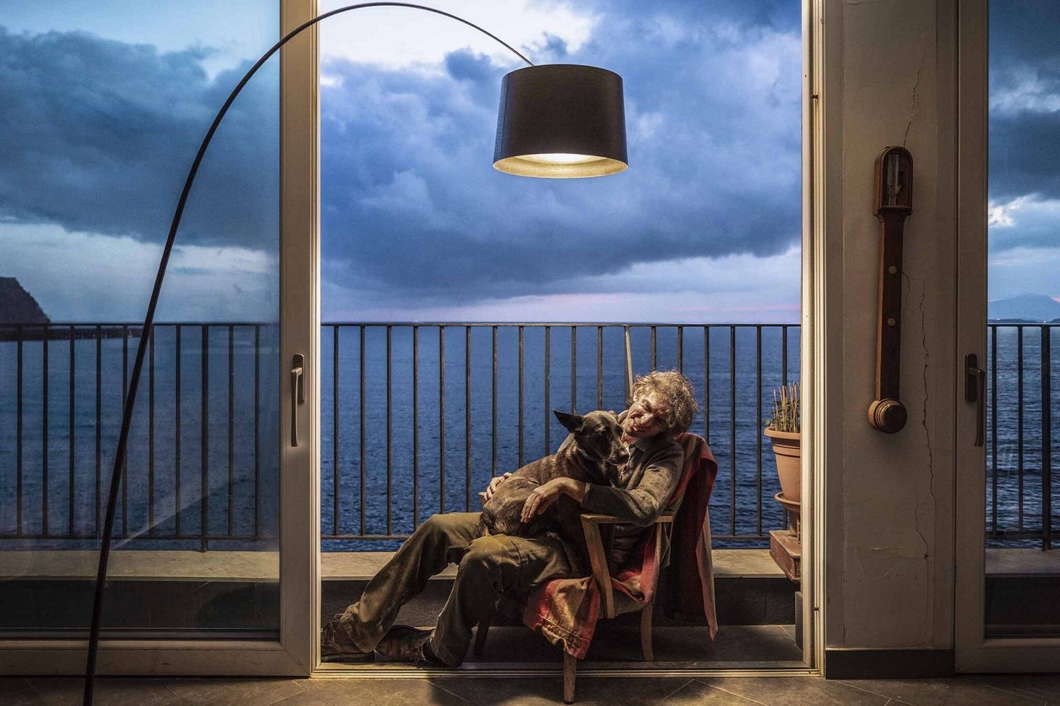 Twiggy Stehleuchte von Foscarini: Frau mit Hund sitzt unter der modernen Bogenlampe mit Schirm am Meer.