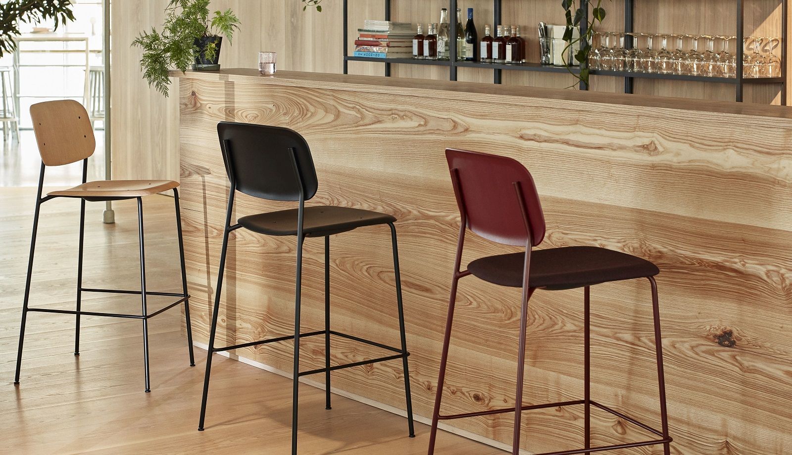Drei Hay Soft Edge Barhocker in Holz, Schwarz und Rot vor einer hölzernen Bar.