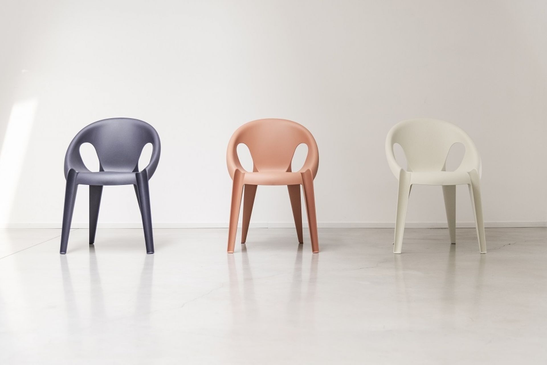 Drei Bell Chairs von Magis in Grau, Rosa und Weiß, stapelbare Indoor- und Outdoor-Stühle mit Armlehnen.
