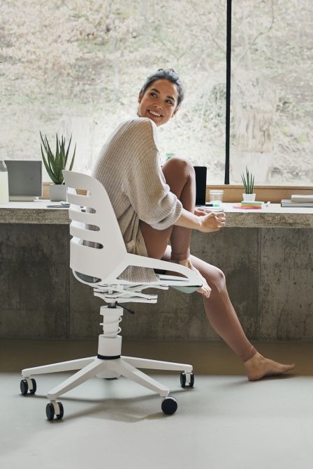 Frau sitzt lächelnd auf einem weißen Numo Task Bürostuhl von Aeris mit Rollen.