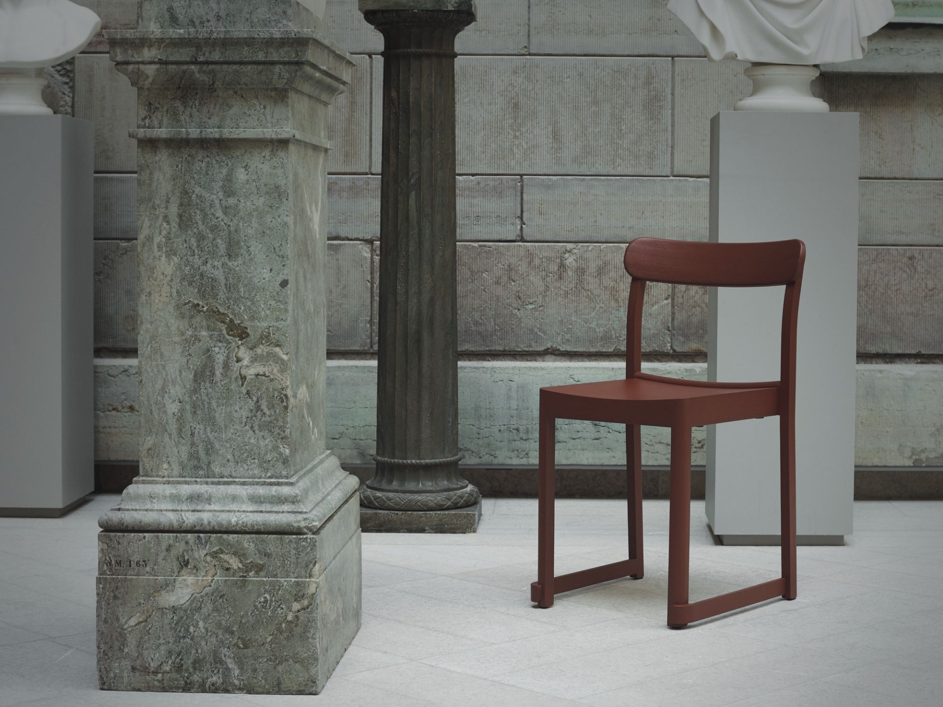 Atelier Chair Stuhl von Artek in Rotbraun vor Säulen und Steinwand.