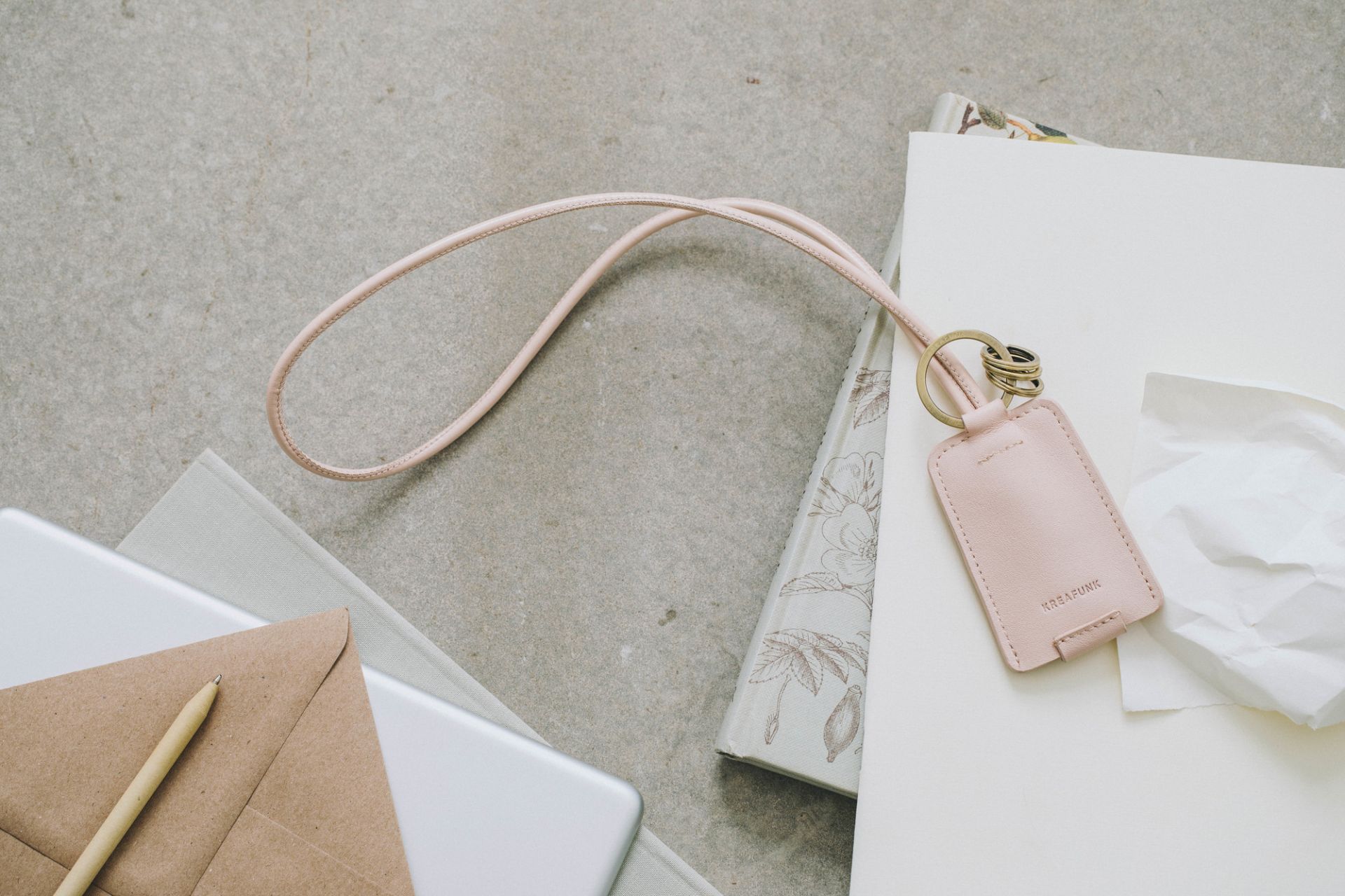 cCHAIN Schlüsselanhänger von Kreafunk mit USB-Kabel in Rosa auf Schreibtisch mit Notizbuch und Umschlag.