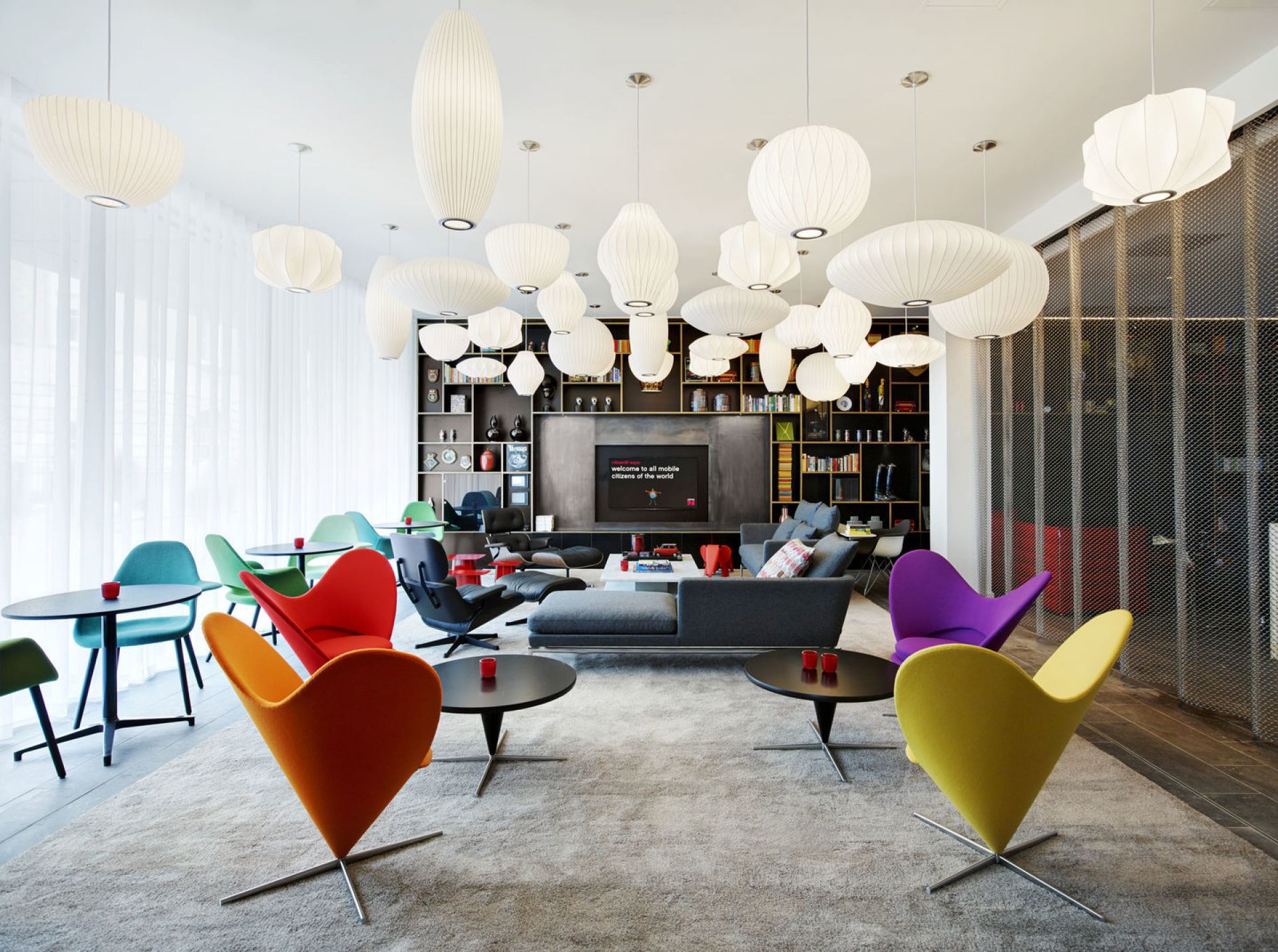 Helle, moderne Lounge mit Vitra Akari Pendelleuchten und bunten Cone Chairs für ein stilvolles Ambiente.