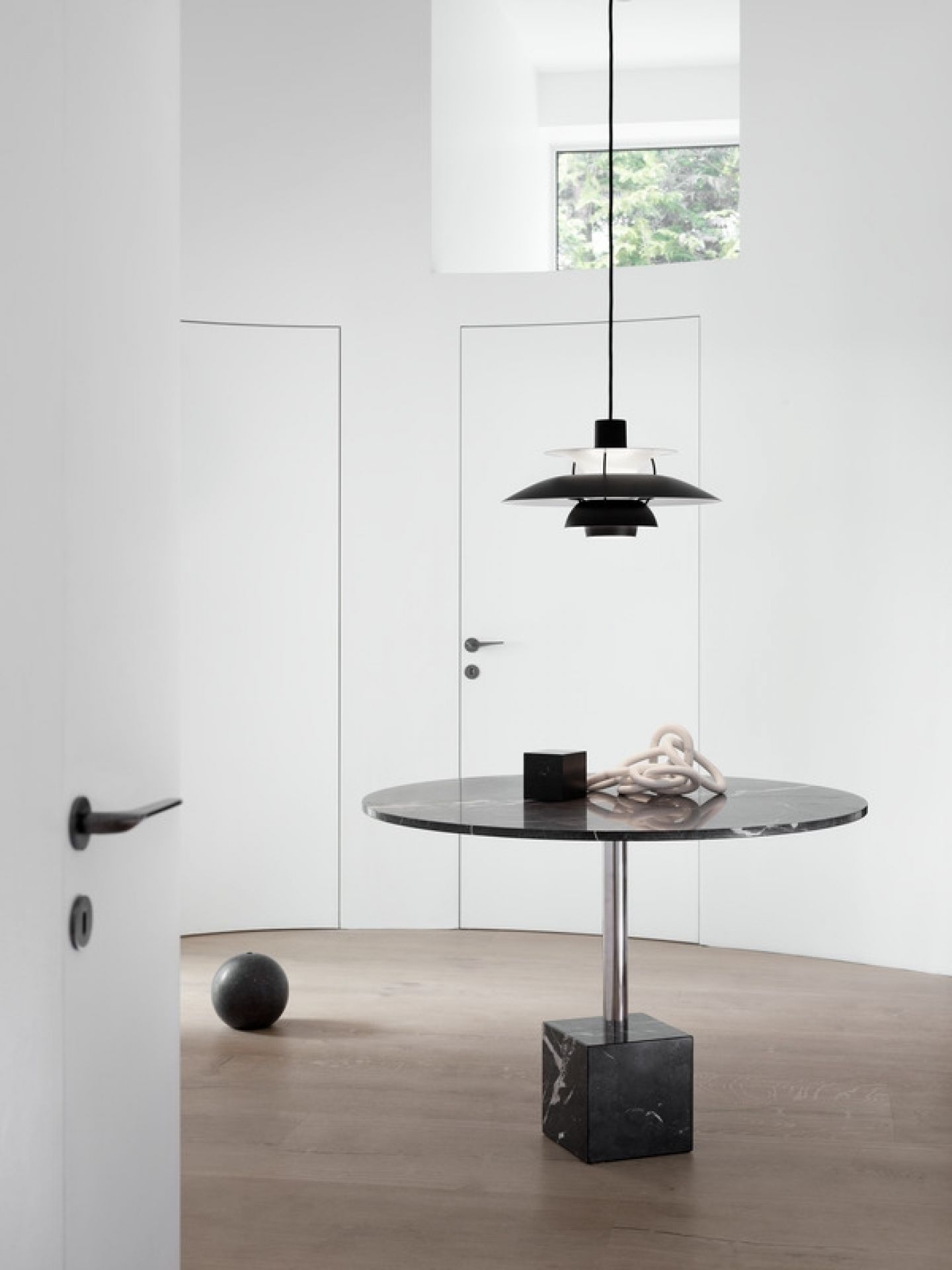 Moderne, schwarze PH 5 Mini Pendelleuchte von Louis Poulsen über einem runden Marmortisch in minimalistischem Interieur.