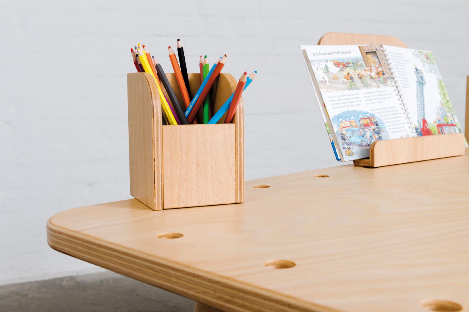 Growing Table Buche Pure Position: Detailansicht mit Stiftehalter, Buchständer und Kinderbuch auf dem Kindertisch.