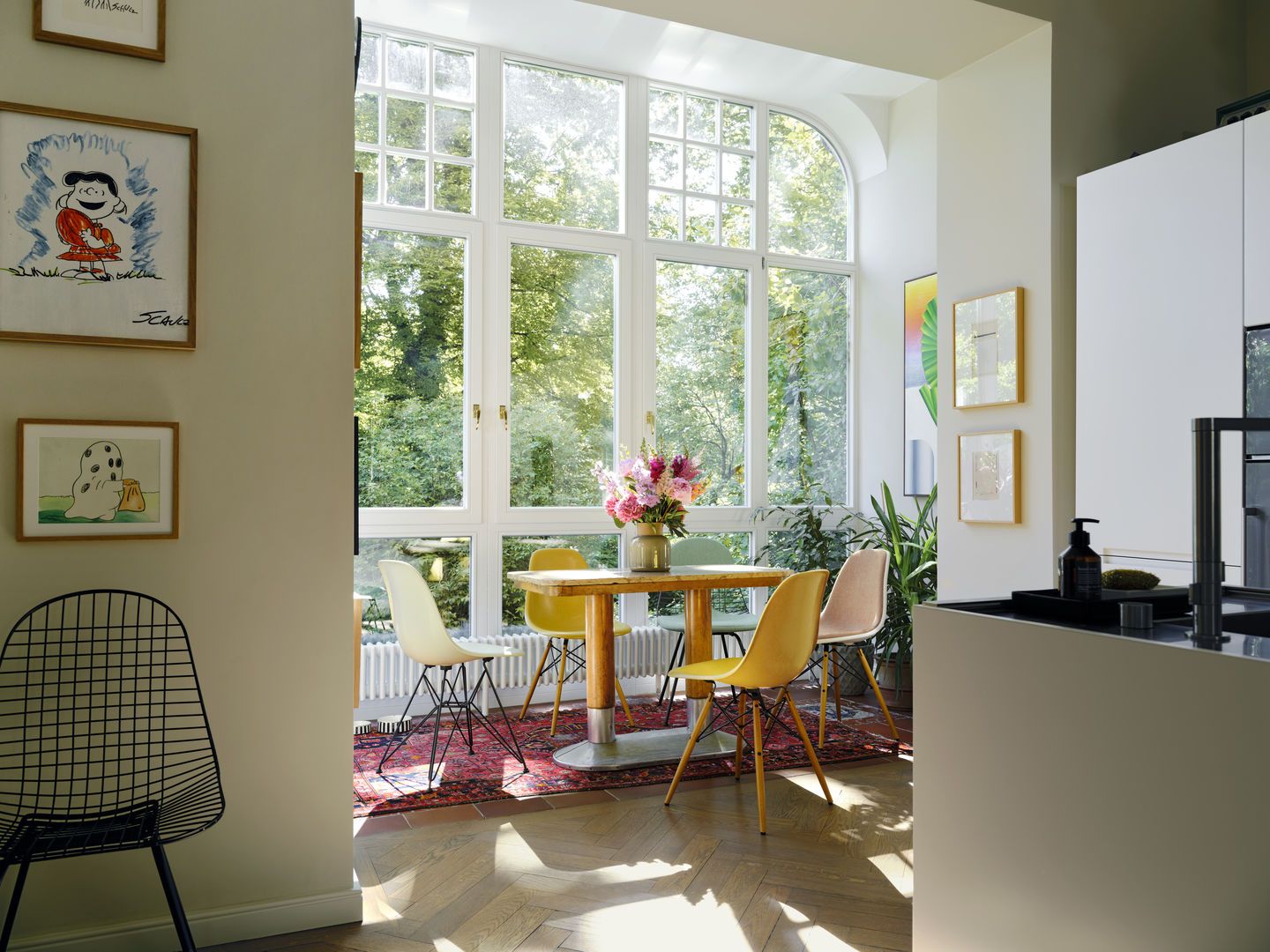 Esszimmer mit Holztisch, bunten Eames Plastic Side Chairs DSW von Vitra und großem Fenster.