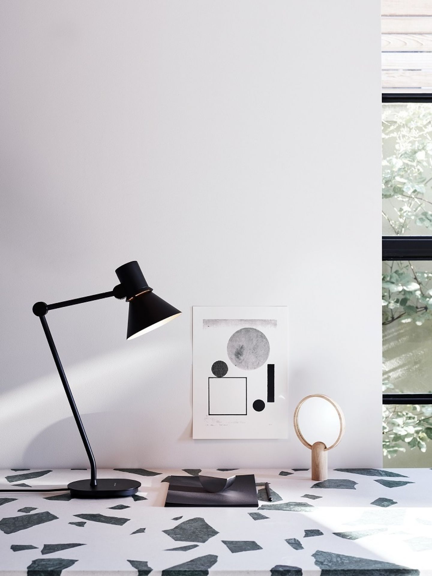 Schwarze Anglepoise Type 80 Tischleuchte auf einem Schreibtisch mit abstraktem Muster und minimalistischer Dekoration.