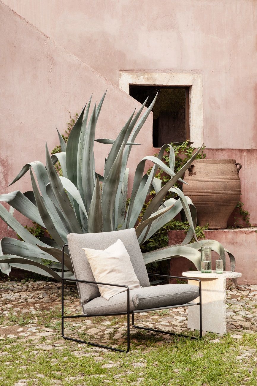 Ferm Living Desert Outdoor Sofa 1-Sitzer in Grau mit Kissen und Beistelltisch im Garten.