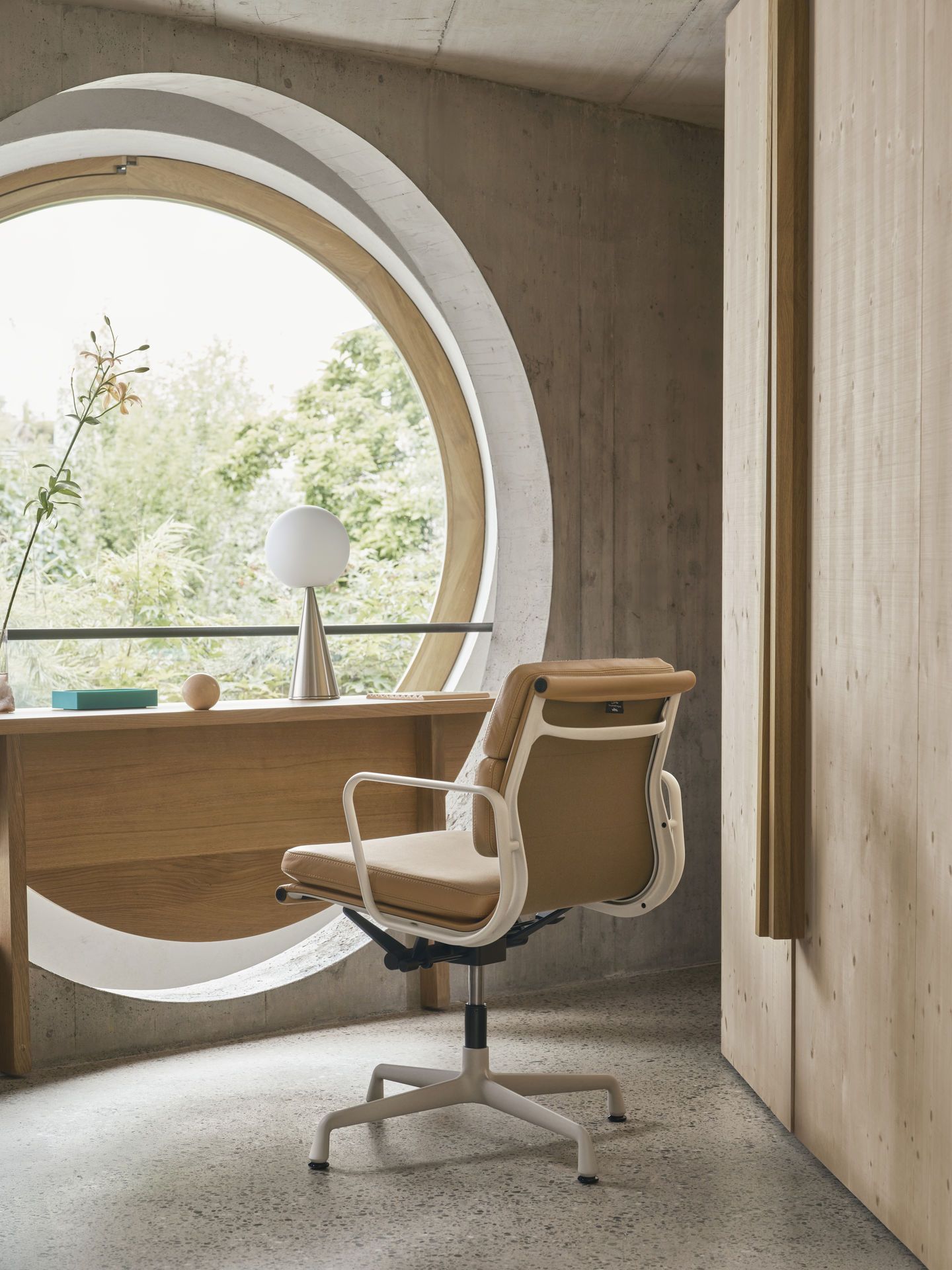 Vitra Soft Pad Chair EA 231 in Beige vor einem runden Fenster im modernen Büro.