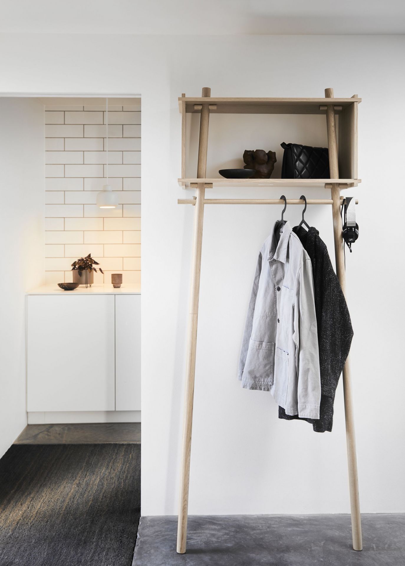 Hellele Holzgarderobe mit Ablage, Jacken, Handtasche und Kopfhörer; im Hintergrund Stone Pendant Pendelleuchte klein von Woud sichtbar.