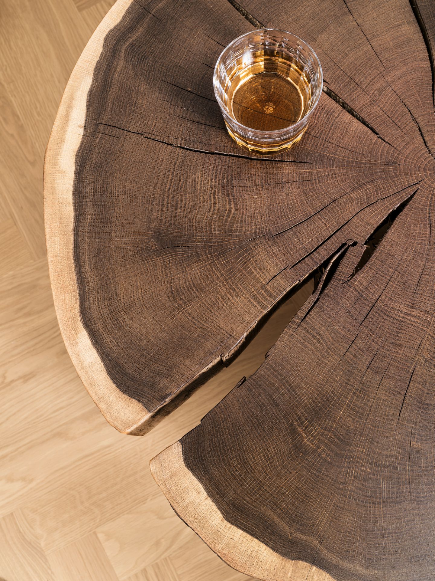 Detailaufnahme Janua Stomp Beistelltisch H52 roh: Massiver Holztisch mit Baumscheiben-Optik und einem Glas Whiskey.