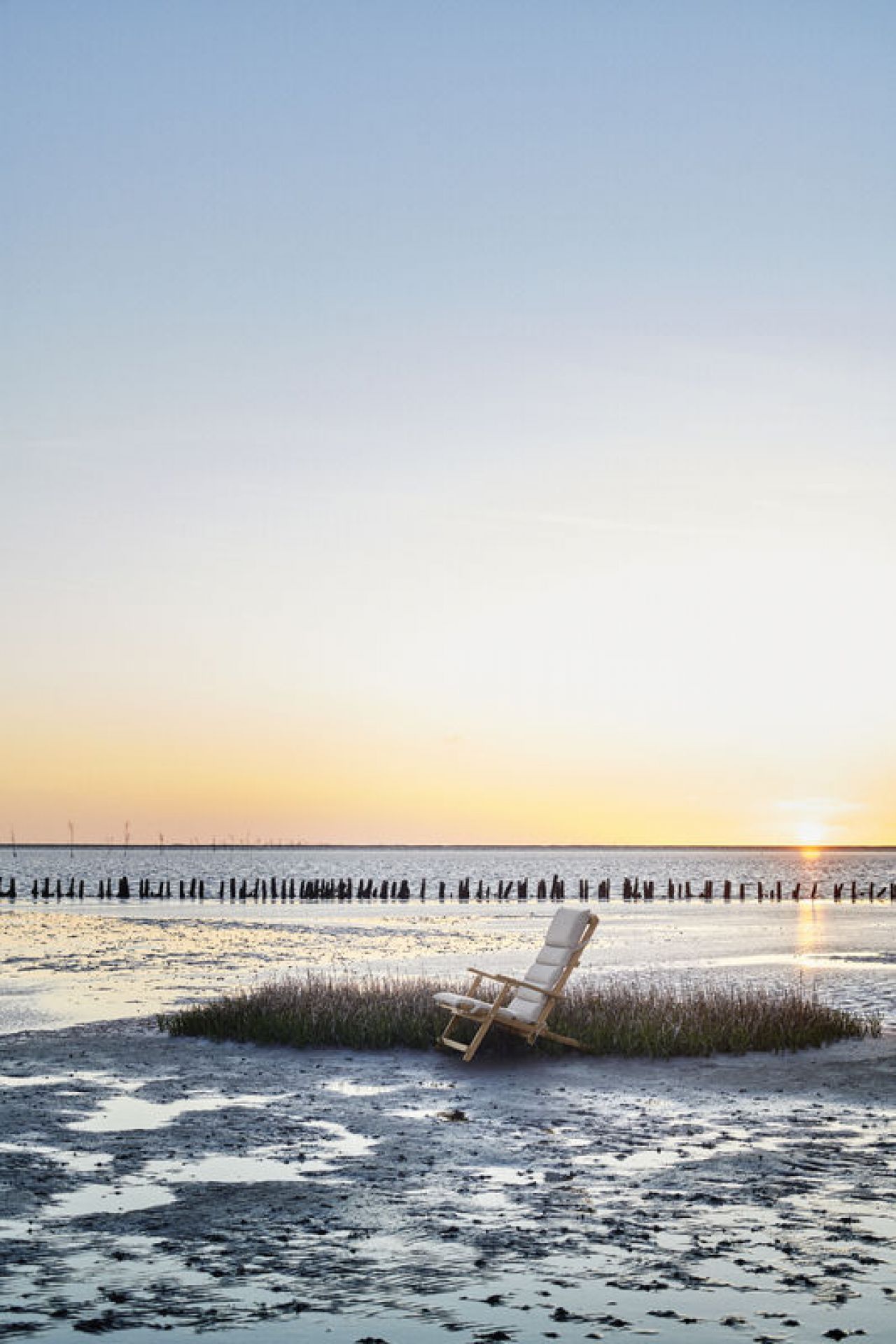 BM5568 Borge Mogensen Liegestuhl mit Kissen von Carl Hansen & Søn am Strand bei Sonnenuntergang.