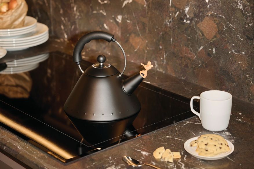 Schwarzer Alessi Wasserkessel 9093 BB auf einem Induktionskochfeld mit Tasse und Keksen.
