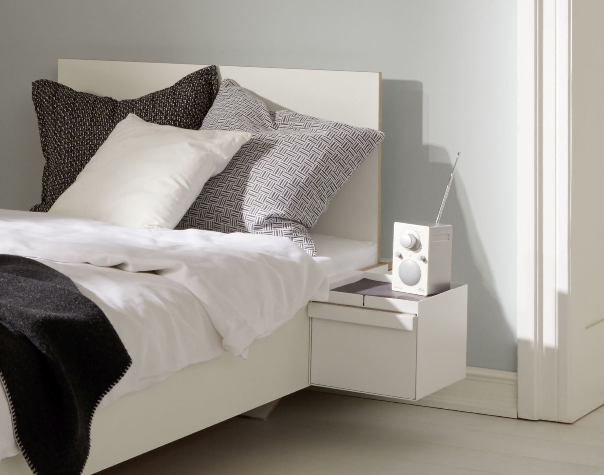 Weißes Flai Add-On Element von Müller Möbelwerkstätten mit Schubkasten als Nachttisch am Bett.