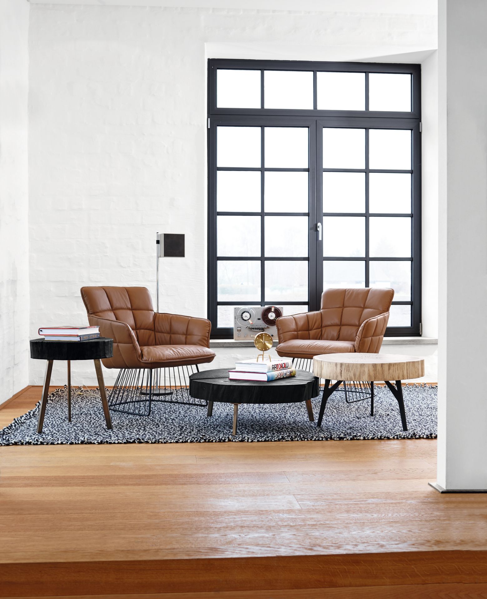 Wohnzimmer mit zwei braunen Sesseln und Janua Stomp Beistelltischen aus rohem Holz und schwarzem Holz.