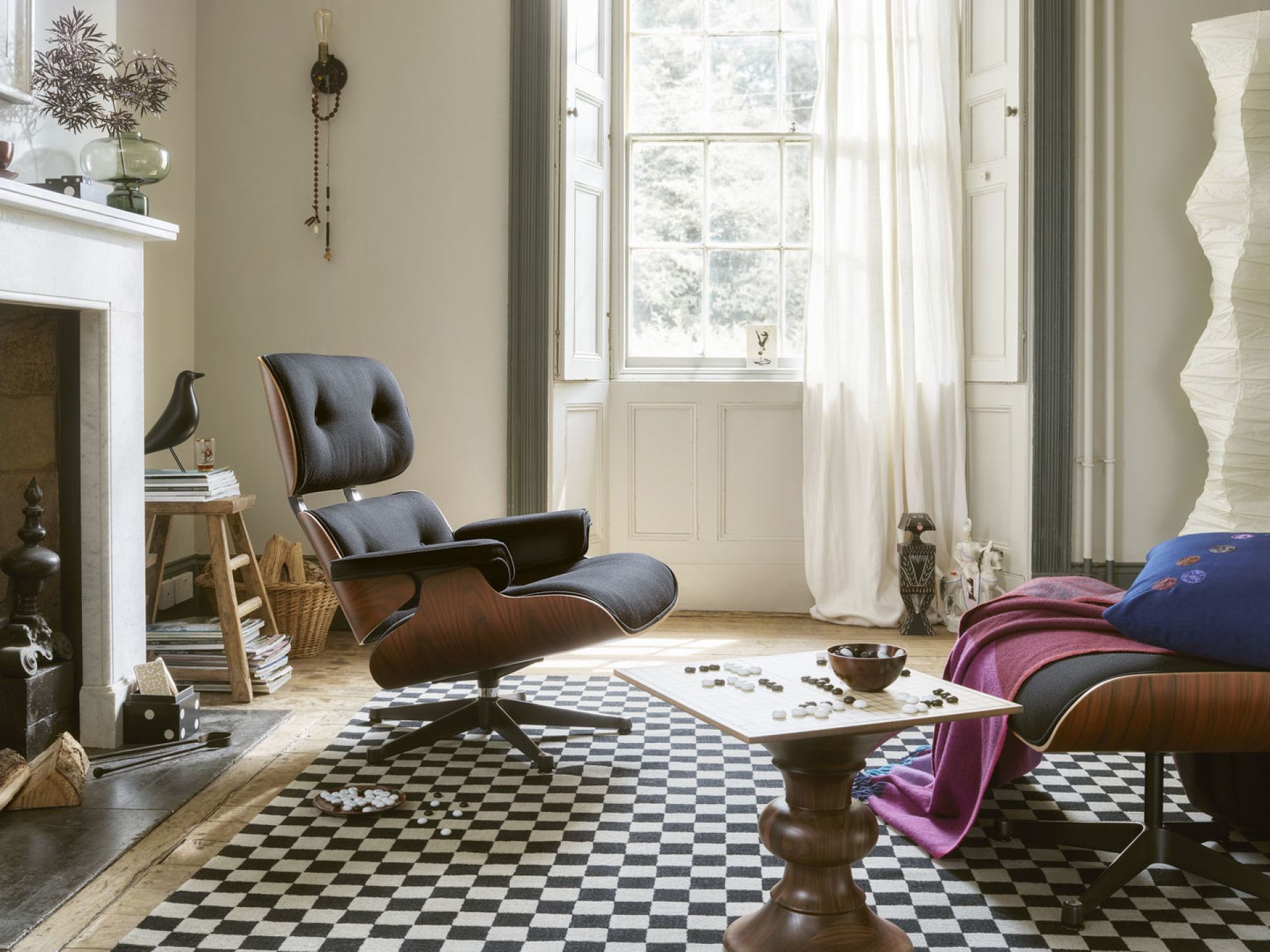 Wohnzimmer-Szene mit Vitra Eames Lounge Chair, Ottoman, Schachbrett-Teppich und einer Wooden Doll Katze als Dekoration.