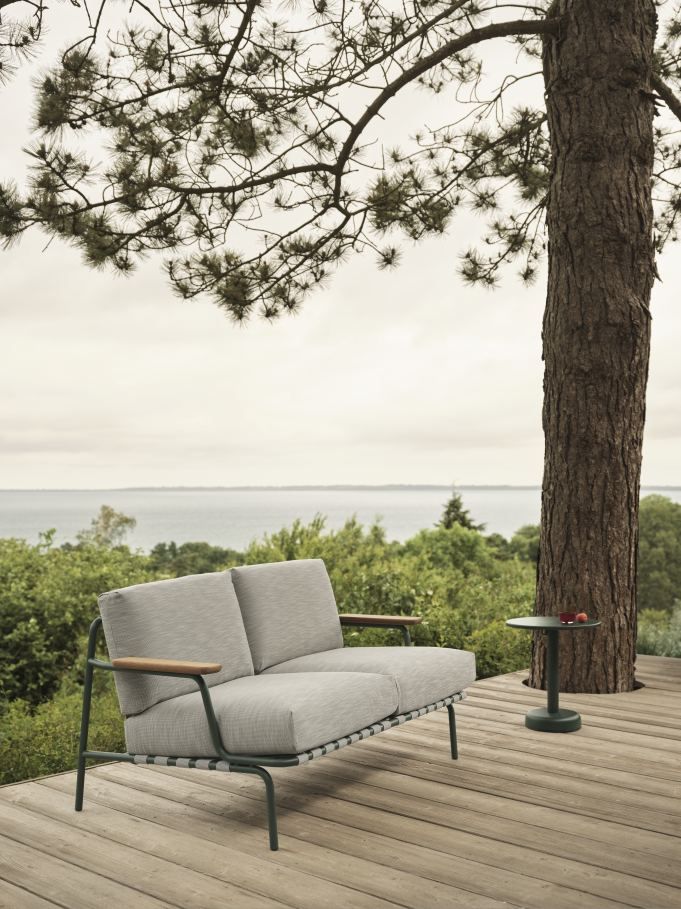 Muuto Settle 2-Sitzer Outdoor Sofa in Grau auf Holzterrasse mit Meerblick und Beistelltisch.