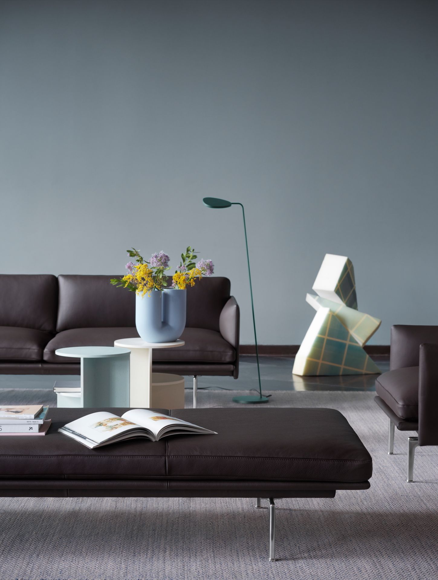 Braunes Muuto Outline Daybed mit Kissen und offenem Buch in modernem Wohnzimmer.