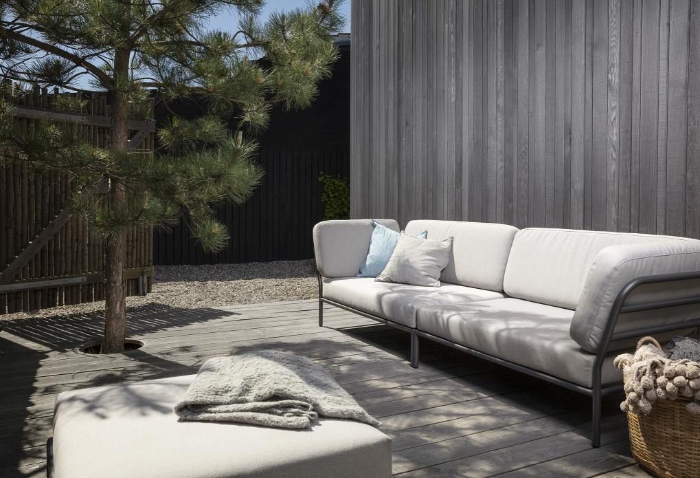 Houe Level Outdoor Sofa Ecke links auf Holzterrasse mit Kissen und Beistelltisch.