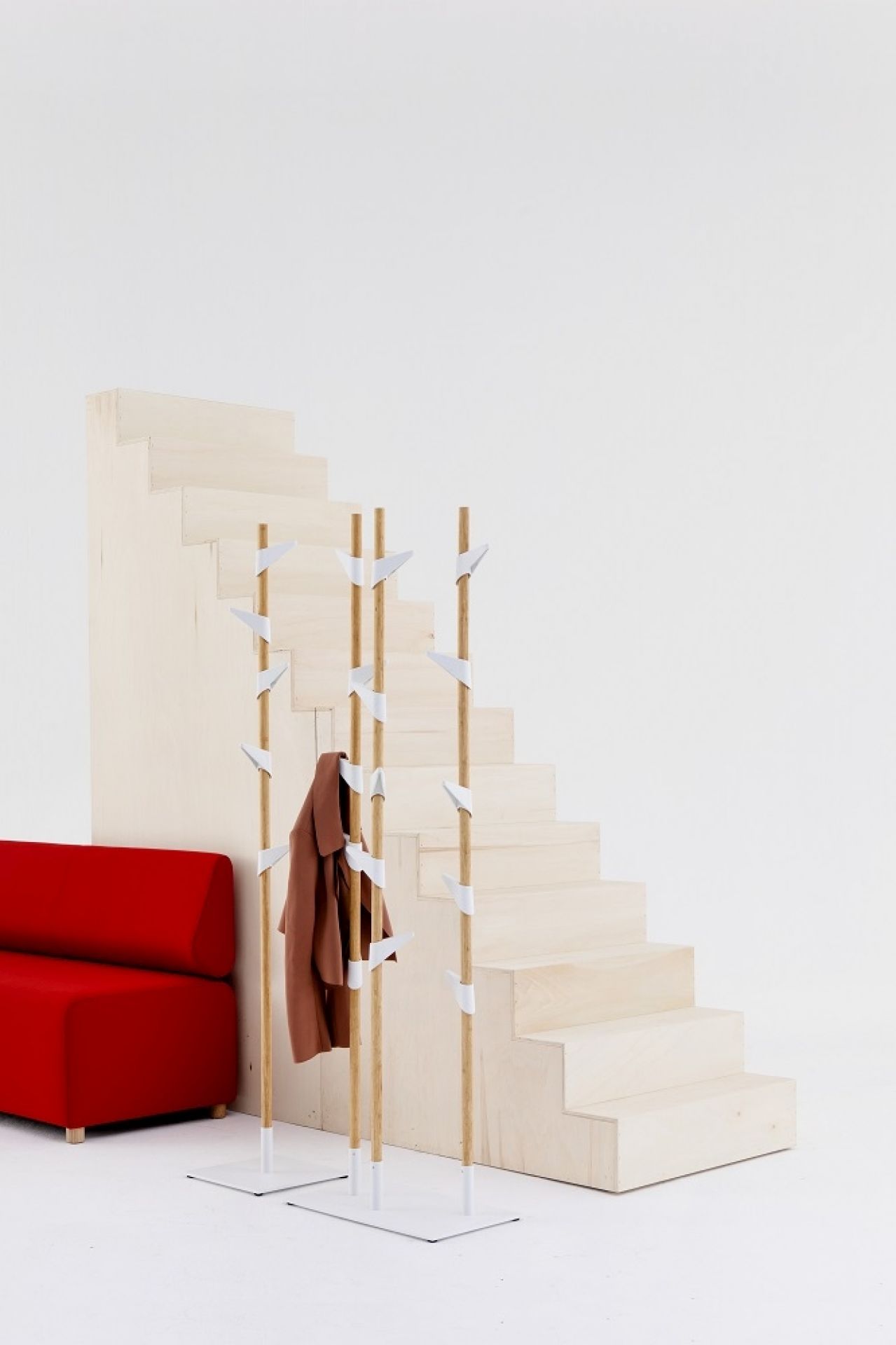 Freistehende Cascando Garderobe aus Bambus mit weißem Metallfuß, vor Treppe und rotem Sofa.