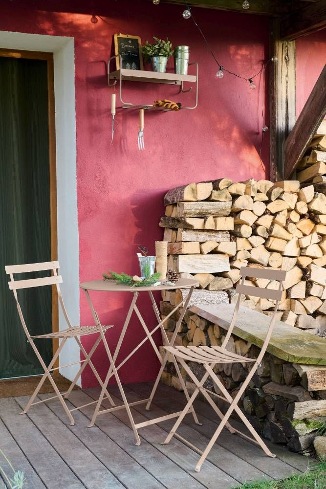 Fermob Picolino Wandregal und Gartenset: Outdoor-Szene mit Tisch, Stühlen, Regal und Holzstapel an roter Hauswand.