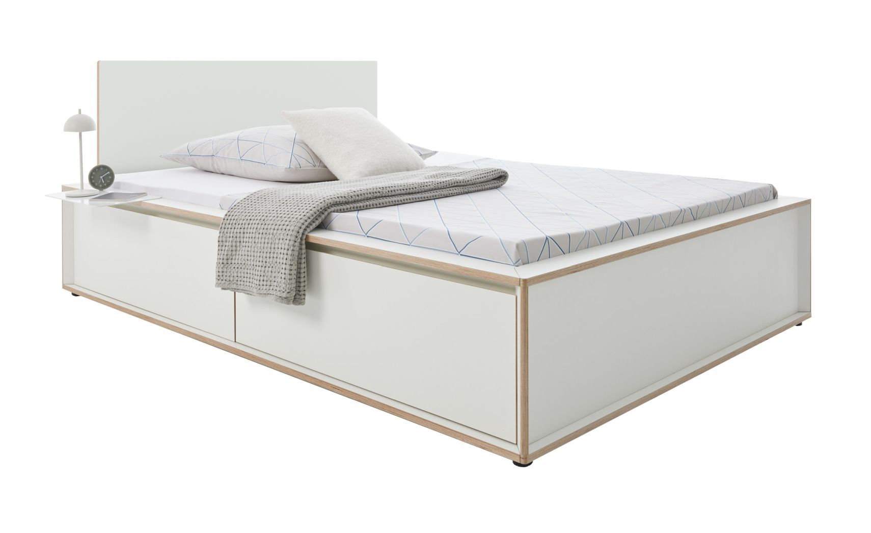 Spaze Bett von Müller Möbelwerkstätten in Weiß mit Schubladen, Nachttisch, Kissen und Decke.